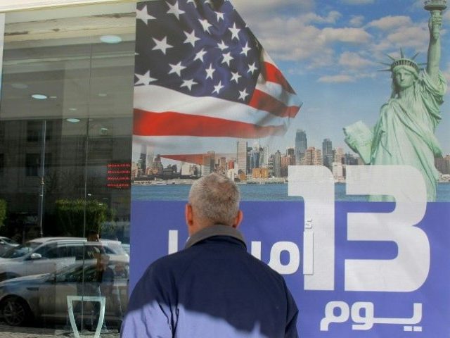 An Iraqi man stands next to an ad for a 13-day trip to the United States at a travel agenc