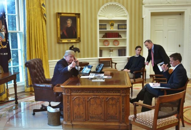 US President Donald Trump (L), seen through an Oval Office window, gives a thumbs up as he