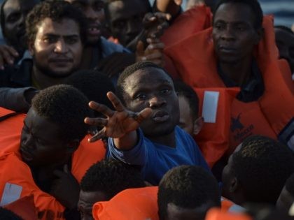 TOPSHOT - Migrants and refugees seated on a rubber boat grab life jackets thrown by member