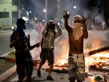 Youths with T-shirts covering their faces gesture next to a barricade in Vitoria, Espirito