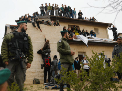 Israeli security forces stand guard as youths supporters of settlements sit on the rooftop