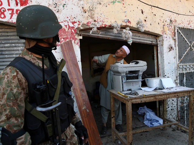 TOPSHOT - A Pakistani soldier stands guard as a shopkeeper examines damage at the site of