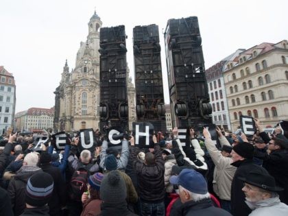 TOPSHOT - Demonstrators hold up posters reading "hypocrisy" as they protest against an installation made of buses titled "Monument" by Syrian-born artist Manaf Halbouni erected at the Neumarkt square close to the Frauenkirche (Church of Our Lady) in Dresden, eastern Germany, on February 7, 2017. The artwork, that aims to …