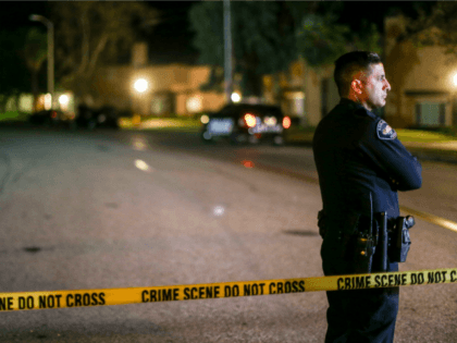 A police officer stands guard inside an area roped off with crime scene tape near a home b