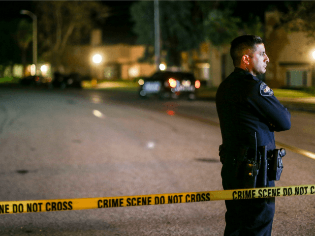 A police officer stands guard inside an area roped off with crime scene tape near a home b