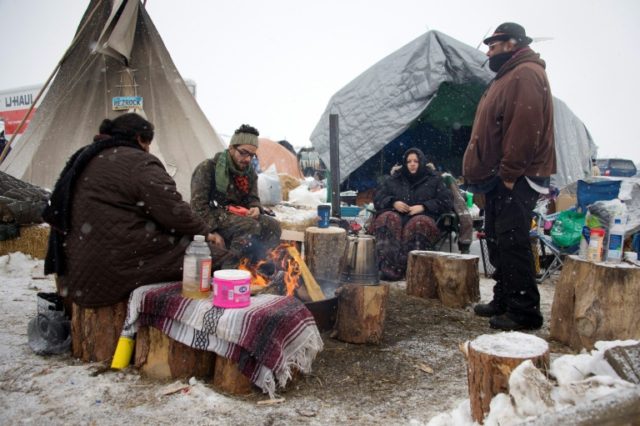 Activists sit around a camp fire as it snows at Oceti Sakowin camp on the edge of the Stan