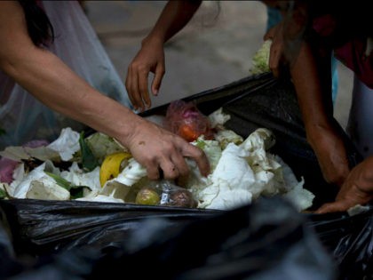 In this June 2, 2016 photo, people search a garbage bag for vegetables and fruit outside a supermarket in downtown Caracas, Venezuela. Unemployed people picking through food tossed out by nearby shops are frequently joined by small business owners, college students and pensioners, people who consider themselves middle class. Living …