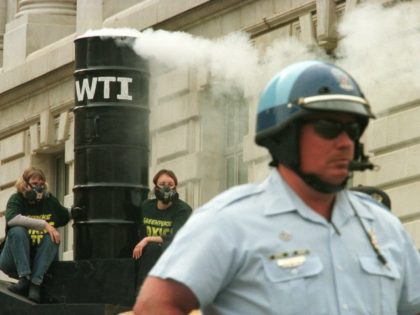A police officer stands guard as two Greenpeace demonstrators, left, chain themselves to a mock incinerator smokestack atop a bus during a protest October 25, 2000 outside the Environmental Protection Agency in Washington. Activists chained themselves to a bus outside the EPA building Wednesday to protest an Ohio incinerator that …