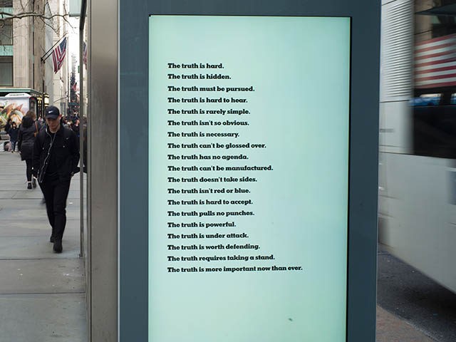 People walk past an electronic board displaying an advertisement by the New York Times, in