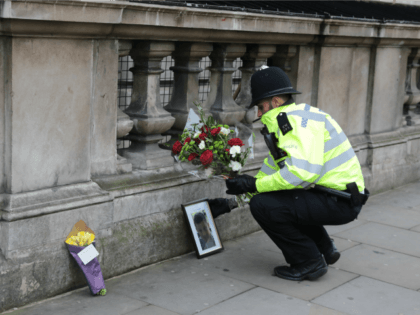 A police officer lays a floral tribute given by a member of the public beside a photo of PC Keith Palmer, the policeman who was stabbed to death as he guarded the Palace of Westminster from a terrorist in yesterday's attack on March 23, 2017 in London, England.
