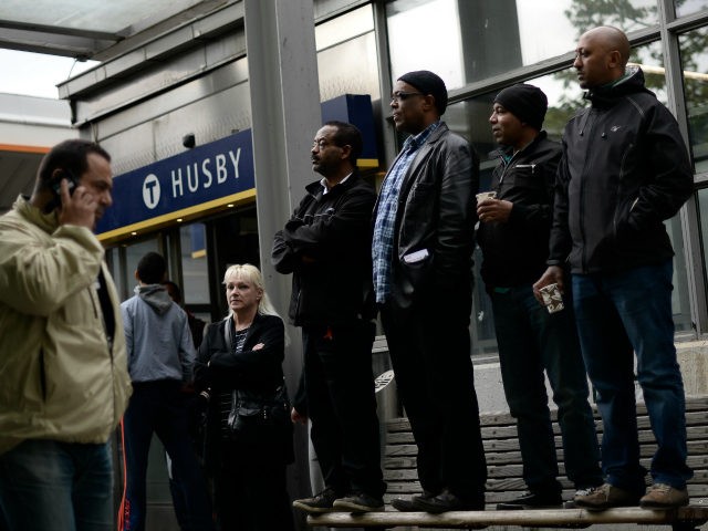 People stand on a street bench next to Husby subway station as they attend a demonstration