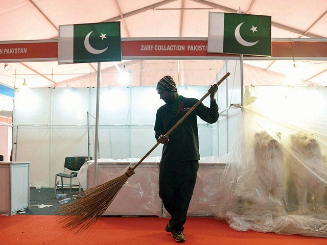 An Indian sweeper cleans the red carpet in the front of Pakistani flags which were on disp