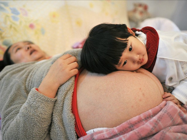 Li Yan (L), pregnant with her second child, lies on a bed as her daughter places her head