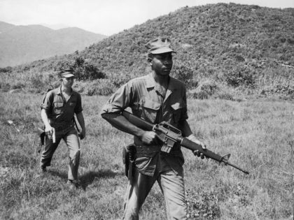 Soldiers Lance Corporal Murphy (R) and Sergeant Paige patrol a jungle area, carrying a rif