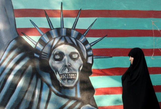 An Iranian woman walks past a mural on the wall of the former US embassy in Tehran