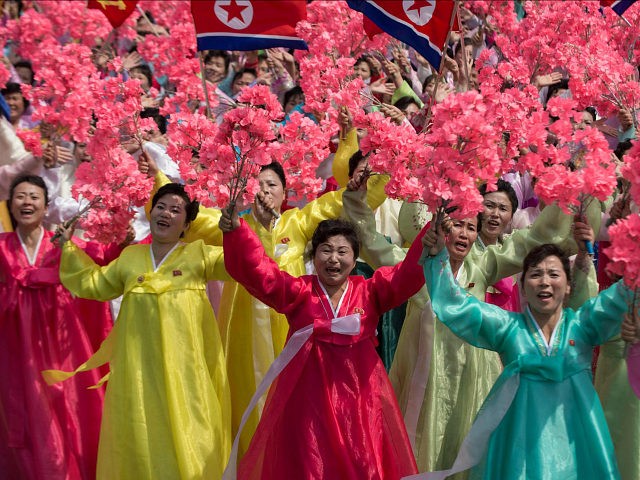 Women wearing traditional Korean dress wave flowers and shout slogans as they pass North K