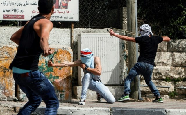 Palestinian protesters use slingshots to hurl stones towards Israeli security forces durin
