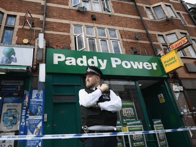 A police officer stands outside a block of flats over shops in East Ham, one of which has