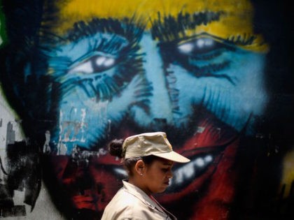 TOPSHOT - A Bolivarian militia member walks by a graffiti of the late Venezuelan President