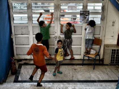 Children stand inside the entrance of an abandoned school used by volunteers for hosting Syrian and Afghan refugees in Athens on July 1, 2016. Some 250 people live in self-management in the school of Athens city center, closed for three years. The families occupy three floors of the building, and …