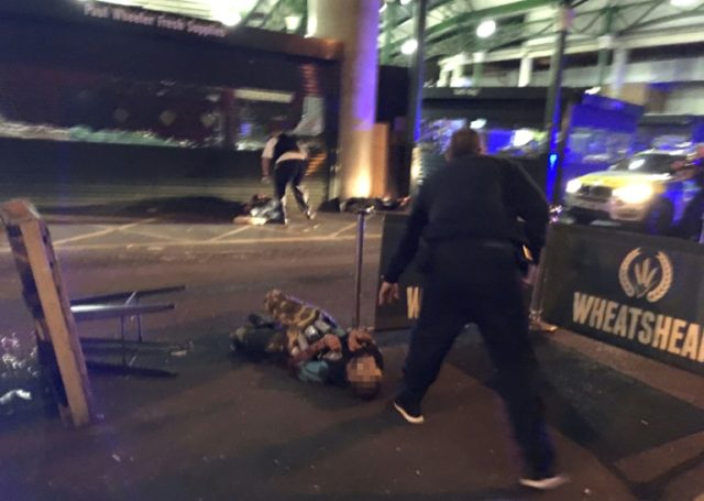 Armed police stand over what is believed to be a suspect (face pixelated) shot at the scen