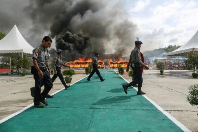 Myanmar police walk near the site where confiscated drugs were burnt