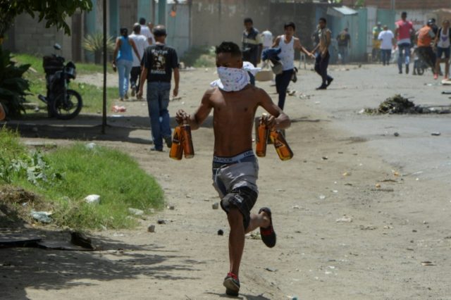 A young man carries stolen alcohol bottles after looting a supermarket in Maracay, Venezue