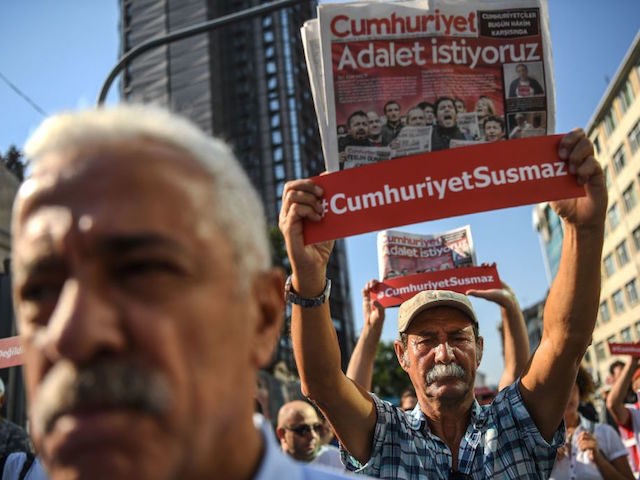 Journalists hold banners reading "Cumhuriyet won't be silenced" and copies