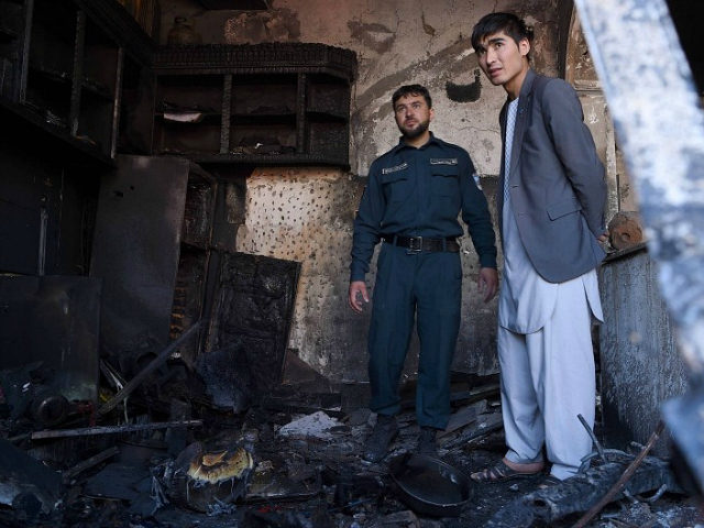An Afghan policeman and a local resident inspect a burnt shop at the site of a car bomb at