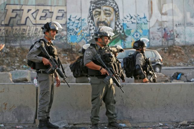 Members of the Israeli border guards stand by a mural showing a graffiti image of late Pal