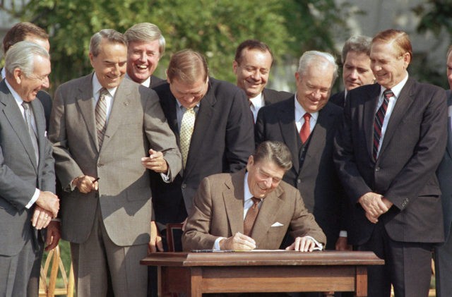 FILE - In this Oct. 22, 1986, file photo, lawmakers watch closely as President Ronald Reagan signs into law a landmark tax overhaul on the South Lawn of the White House in Washington. From left, are: Senate Majority Leader Bob Dole of Kansas, Rep. Raymond McGrath, R-N.Y.; Rep. Dan Rostenkowski, …