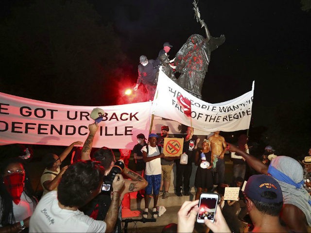 Protesters climb and spray-paint a Confederate monument Sunday, Aug. 13, 2017, at Piedmont Park in Atlanta. The peace monument at the 14th Street entrance depicts an angel of peace stilling the hand of a Confederate soldier about to fire his rifle. Protesters decrying hatred and racism converged around the country …