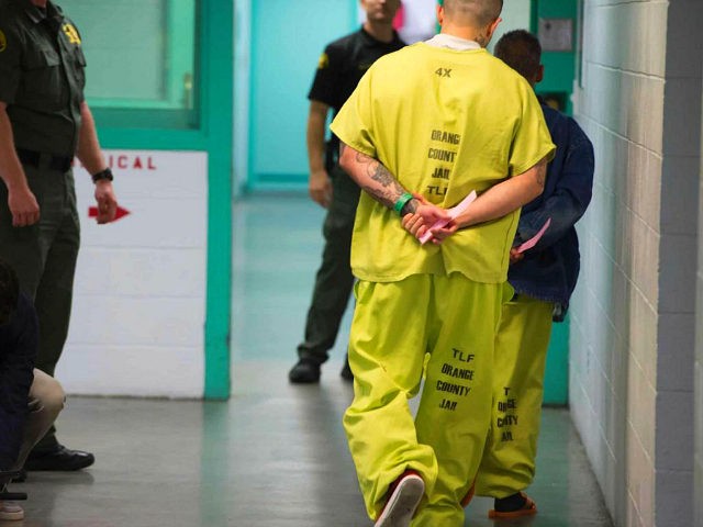 Men wearing neon-colored jail clothes signifying immigration detainees walk down a hall at