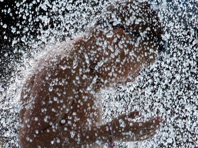 A child enjoys a shower of water at a swimming pool in Beijing, China, Tuesday, July 10, 2