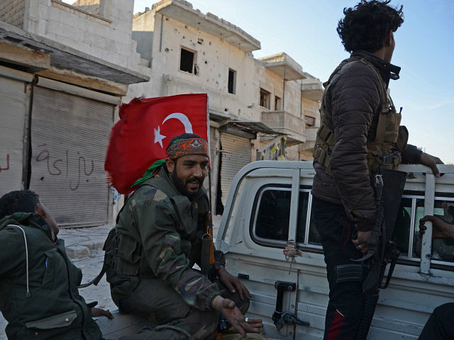 A fighter from the Turkish-backed Syrian rebels holds a Turkish flag as they sit in the back of vehicle in the northwestern border town of al-Bab on February 23, 2017 after they fully captured the town from the Islamic State (IS) group. Al-Bab, just 25 kilometres (15 miles) south of …