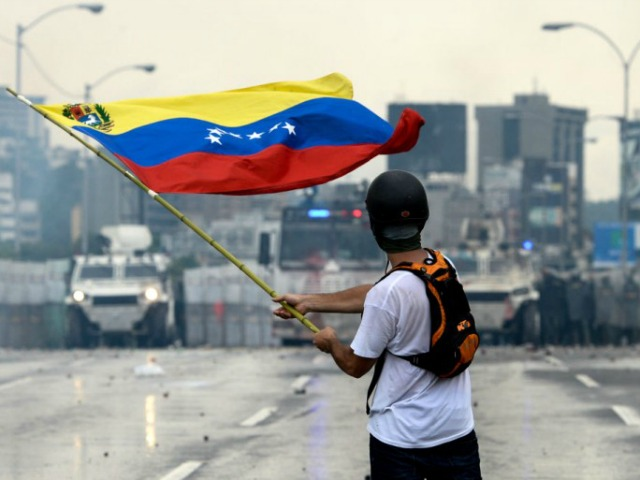 A Venezuelan opposition demonstrator waves a flag at the riot police in a clash during a p