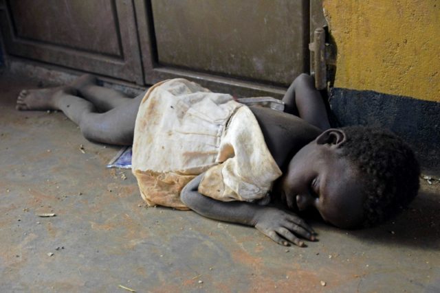 A newly arrived refugee child from South Sudan sleeps on a dirty floor on the Ugandan side