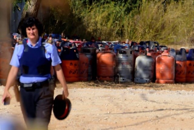 A policewoman walks with dozen of gas bottles in the background in Alcanar, during a searc