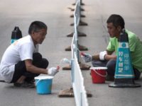 Workers paint a fence on a street in Beijing on September 21, 2017. / AFP PHOTO / FRED DUFOUR (Photo credit should read FRED DUFOUR/AFP/Getty Images)