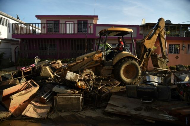 A man bulldozes furniture damaged and debris following Hurricane Maria on a street in Toa