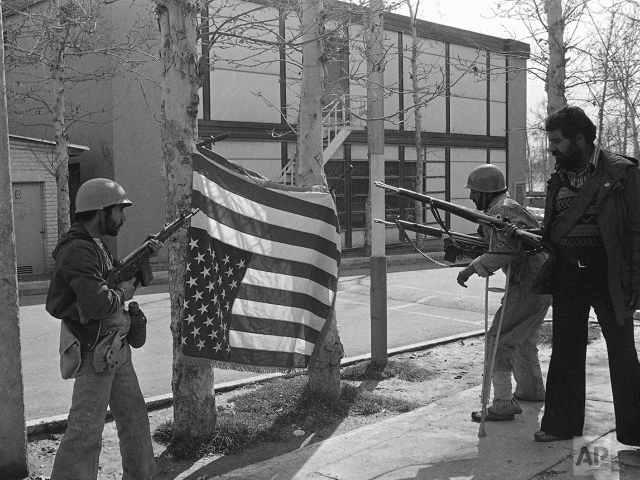 Iran rebels pose with a U.S. flag they bayoneted upside down on trees at Sultanabad Garrison northeast of Tehran, Iran on Feb. 12, 1979. (AP Photo/Saris)