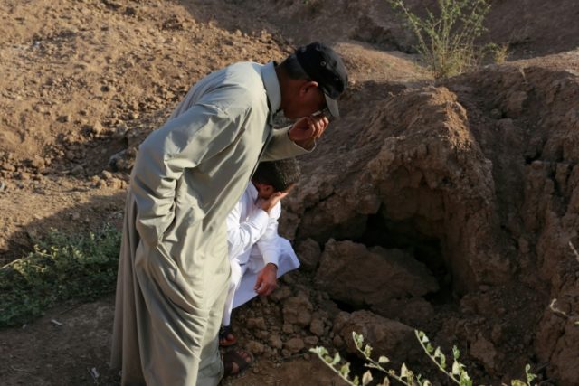 Iraqi men pinch their nose as they inspect the site of a pit containing the bodies of Isla