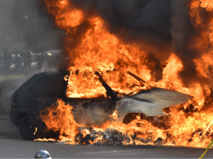 A firefighter stands in front of a burning car during a demonstration against the French g