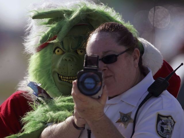The Grinch stands behind a police officer using a laser speed detector