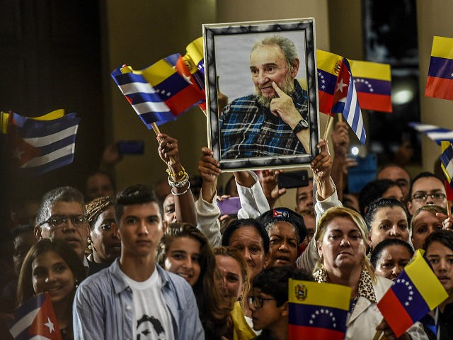 TOPSHOT - Supporters of Venezuelan President Nicolas Maduro wave Cuban flags and a portait of the late Cuban leader Fidel Castro during a ceremony honouring Castro one day after his death, in Caracas, November 26, 2016. / AFP / JUAN BARRETO (Photo credit should read JUAN BARRETO/AFP/Getty Images)