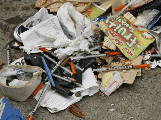 A number of syringes are seen in the remains of a tent city being cleared by city workers