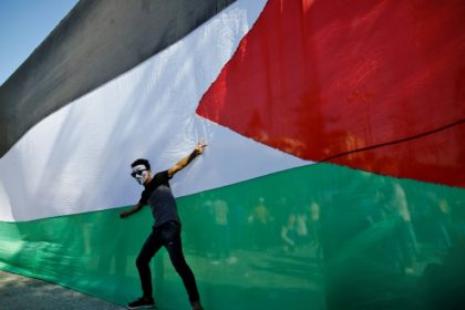 A Palestinian youth celebrates in front of his national flag in Gaza City on October 12, 2017 after rival factions Hamas and Fatah reached an agreement on ending a decade-long split