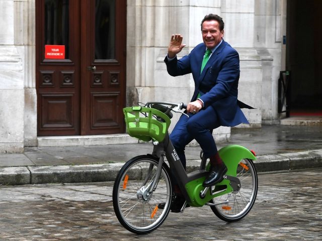 Former Governor of the US State of California Arnold Schwarzenegger waves as he rides a bicycle in Paris on December 11, 2017, on the sidelines of meetings with Mayor of Paris Anne Hidalgo. / AFP PHOTO / ALAIN JOCARD (Photo credit should read ALAIN JOCARD/AFP/Getty Images)