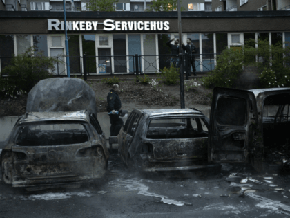 A police officers passes the scene of cars gutted by fire in the Stockholm suburb of Rinke