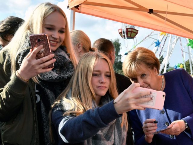 A girl (C) poses for a selfie photo with German Chancellor Angela Merkel (R) as she contin
